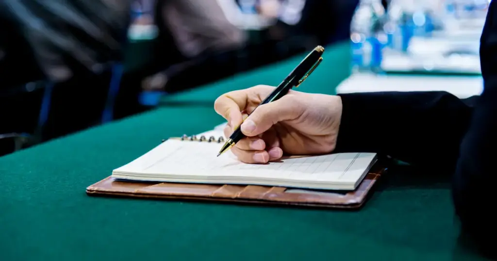 Hand schreibt mit einem Stift in ein Notizbuch auf einem Tisch