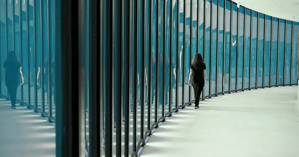 Frau geht durch einen Gang mit Glaswänden, Spiegelungen sind sichtbar