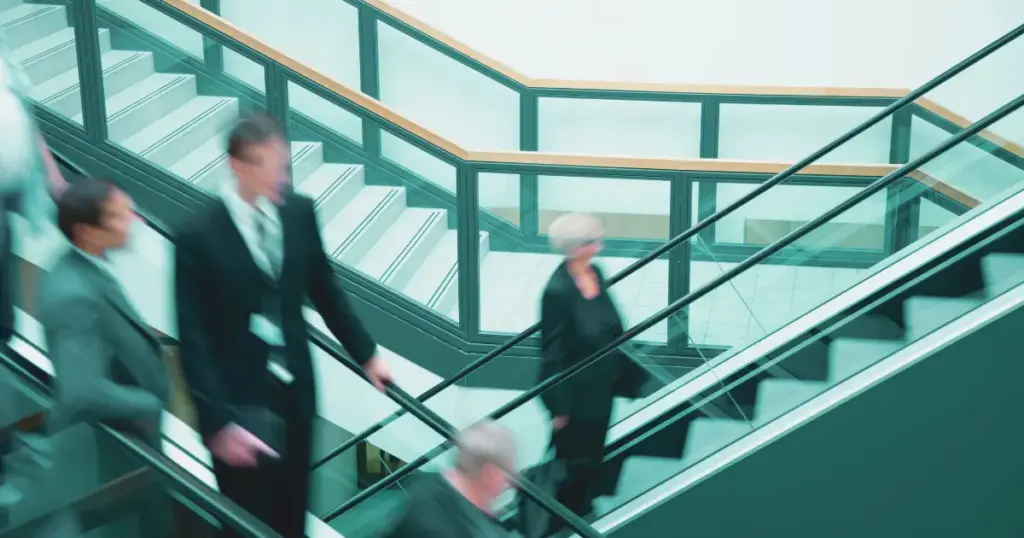 Bewegte, unscharfe Kollegen auf der Rolltreppe als Beispiel für anonymes und reizintensives Arbeitsumfeld für Reflektoren im Beruf